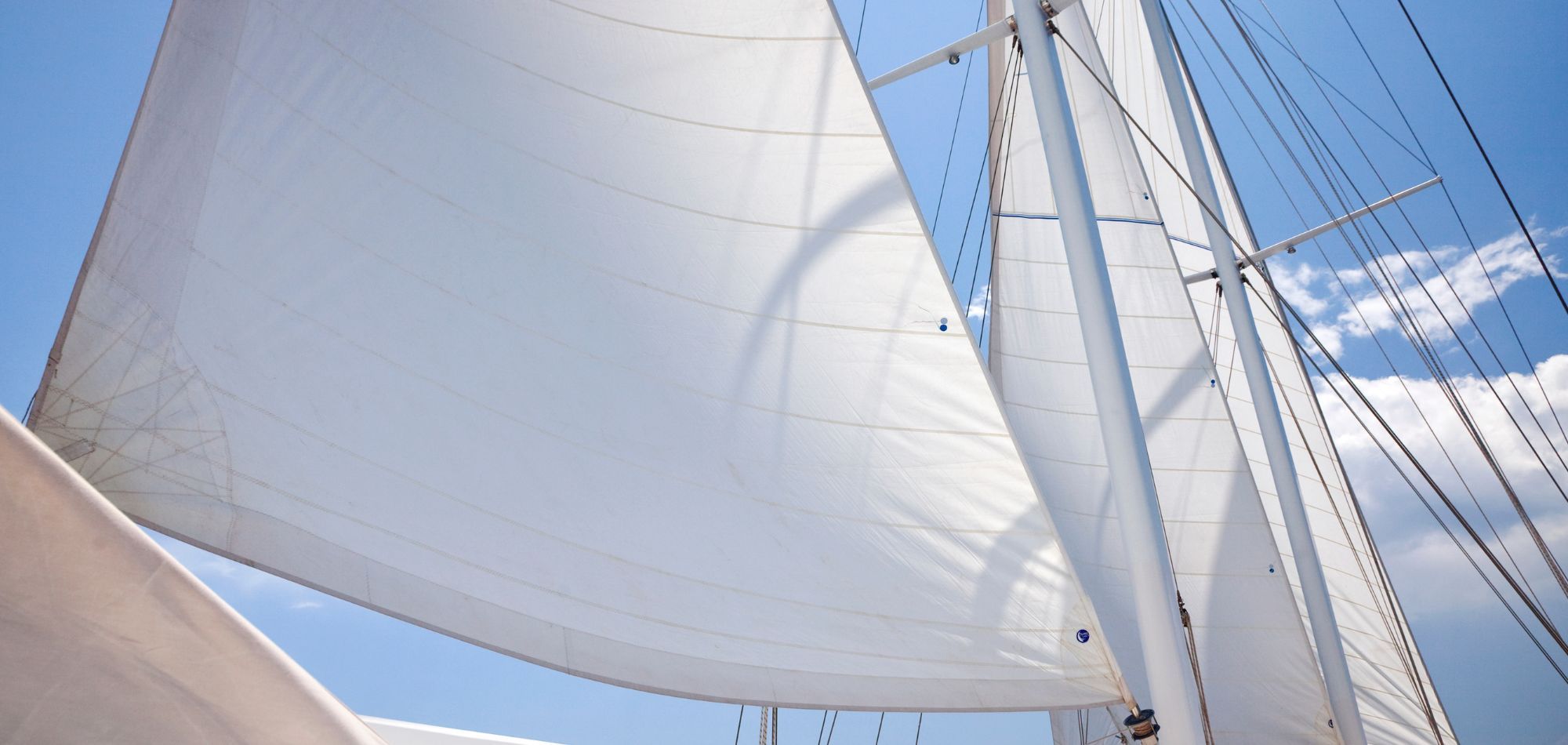 A close-up view of a sailboat's sails, showcasing the intricate fabric and details against a clear sky.