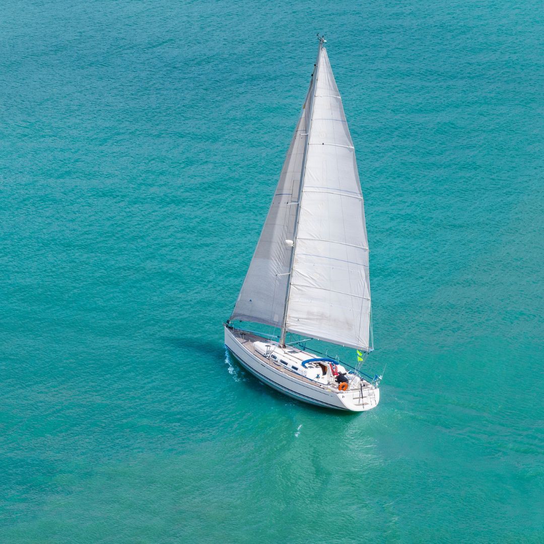 A sailboat glides gracefully across the shimmering ocean waters under a clear blue sky.