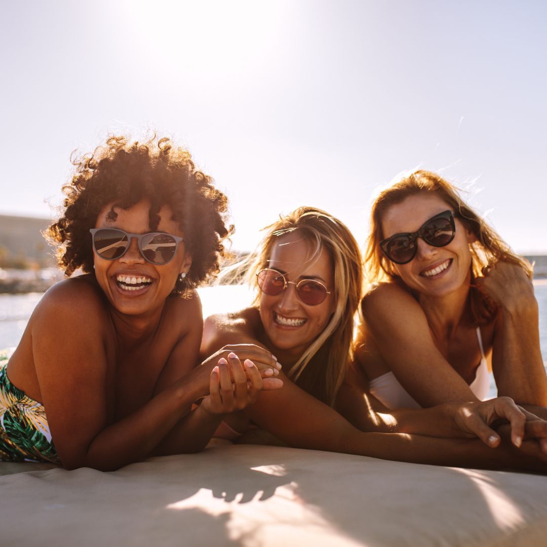 Three women wearing swimsuits and sunglasses enjoy a sunny day on a boat, radiating joy and relaxation.