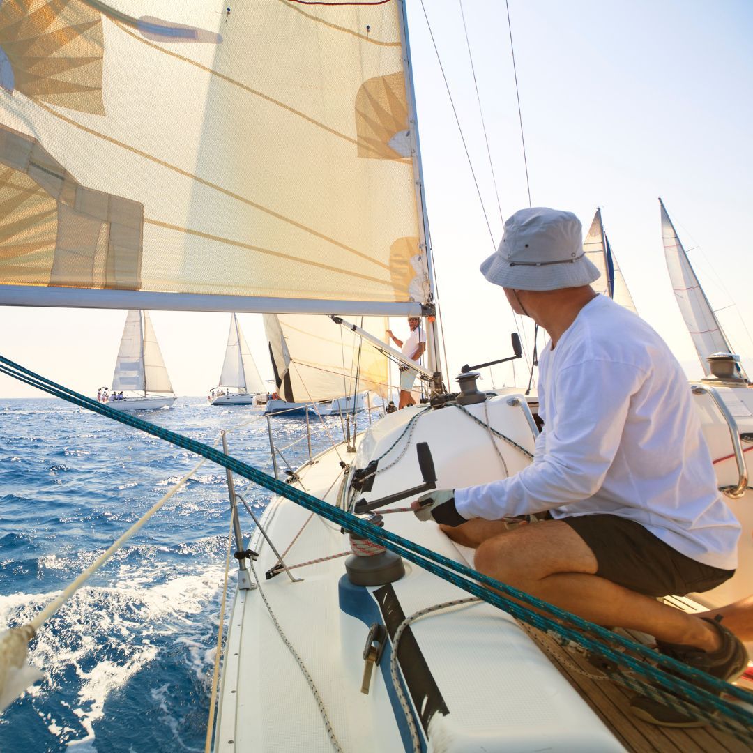 A man sits on the bow of a sailboat, enjoying the serene view of the water and the open sky.