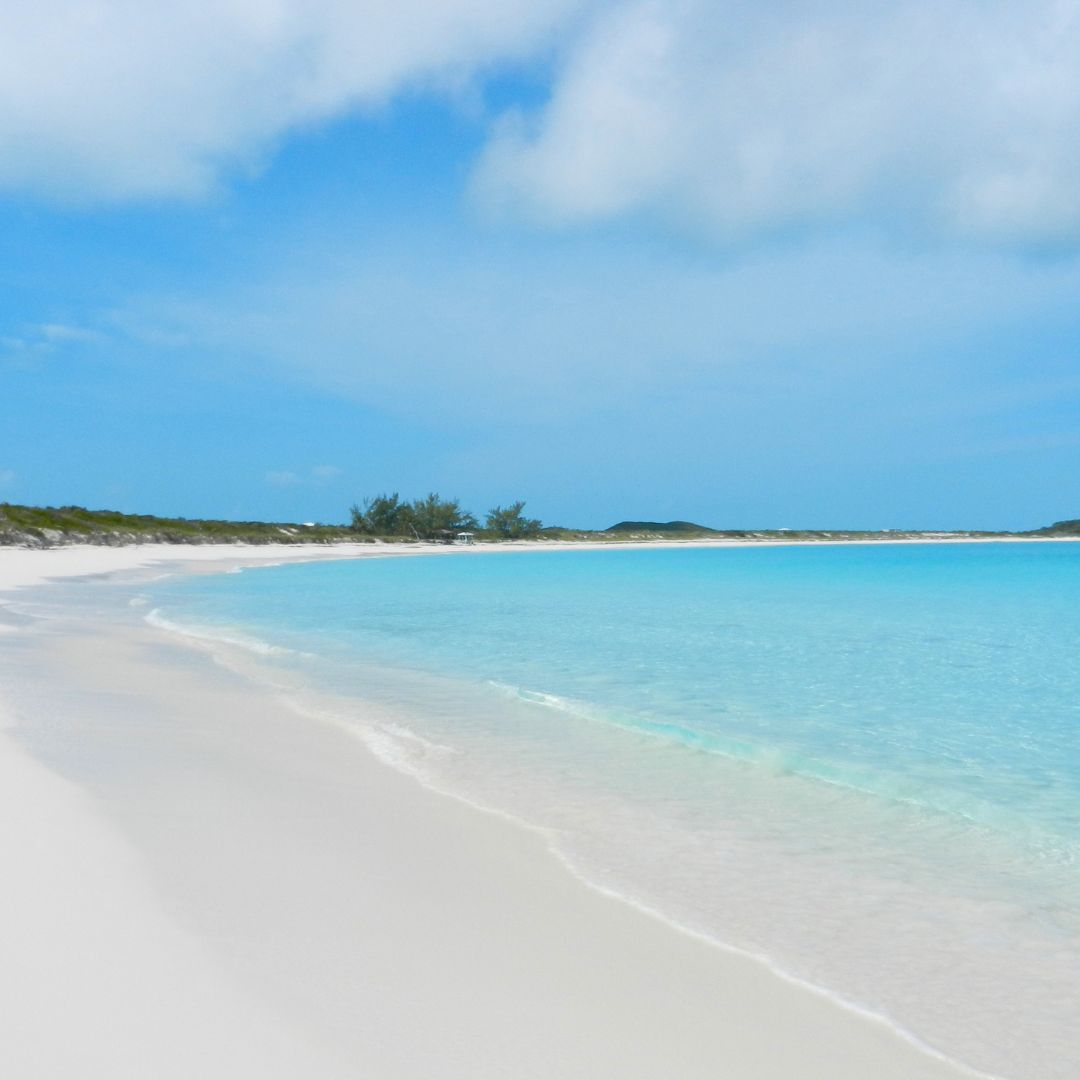 A serene sandy beach featuring clear blue water and pristine white sand under a bright sky.