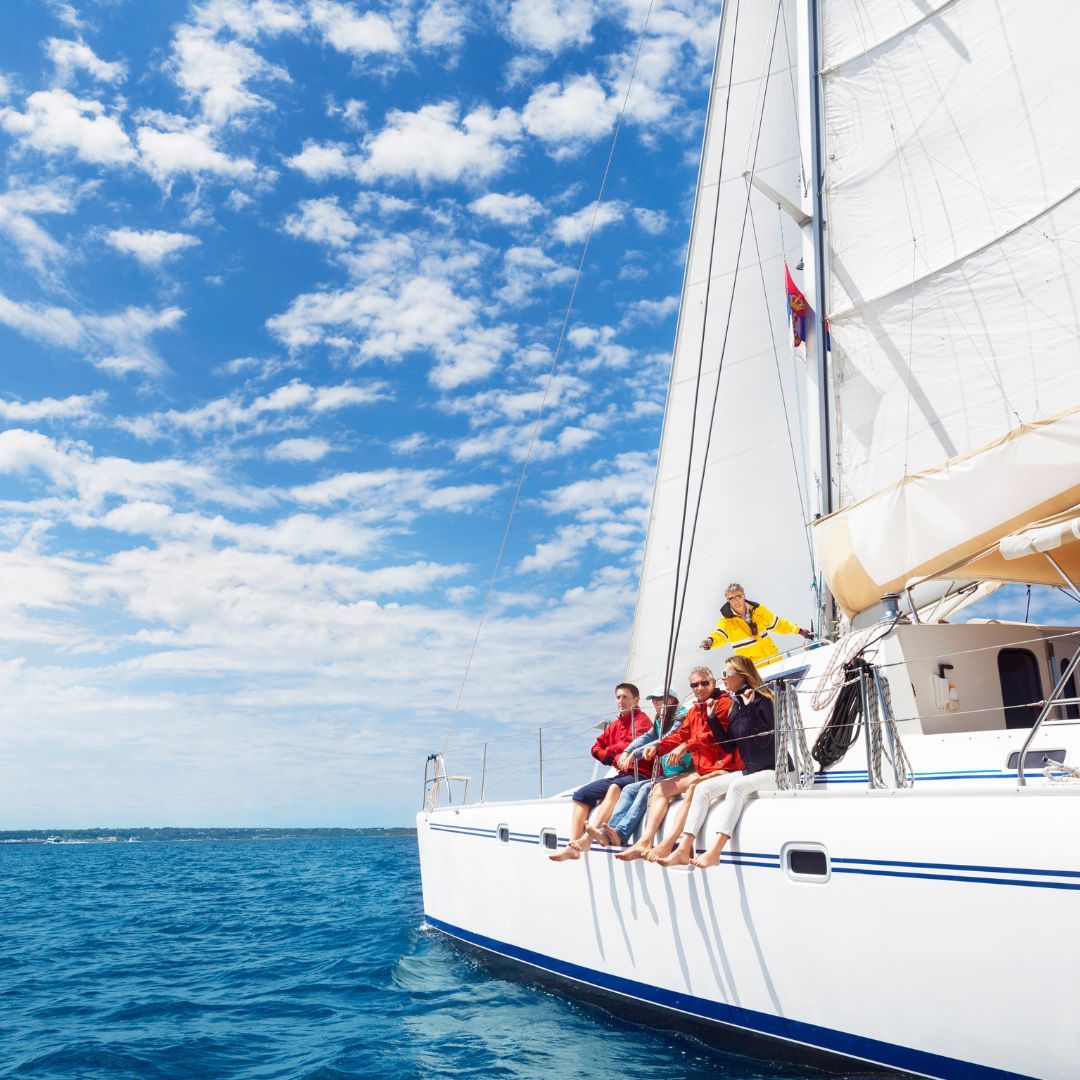 A diverse group of individuals enjoying a sunny day on a sailboat, surrounded by calm waters and clear skies.