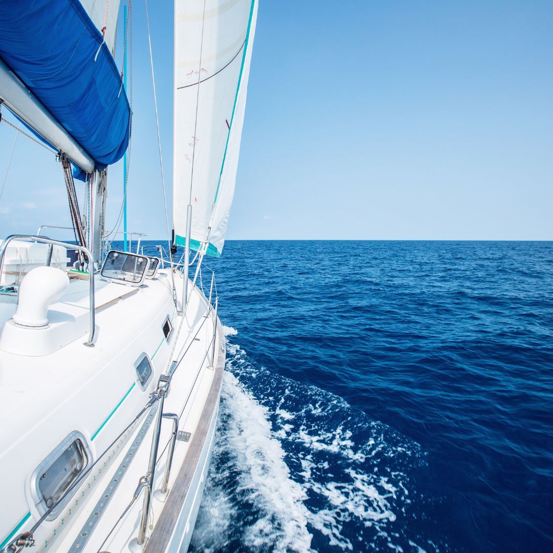 AA sailboat's bow cutting through the ocean waves, showcasing the vast blue sea and clear sky in the background.