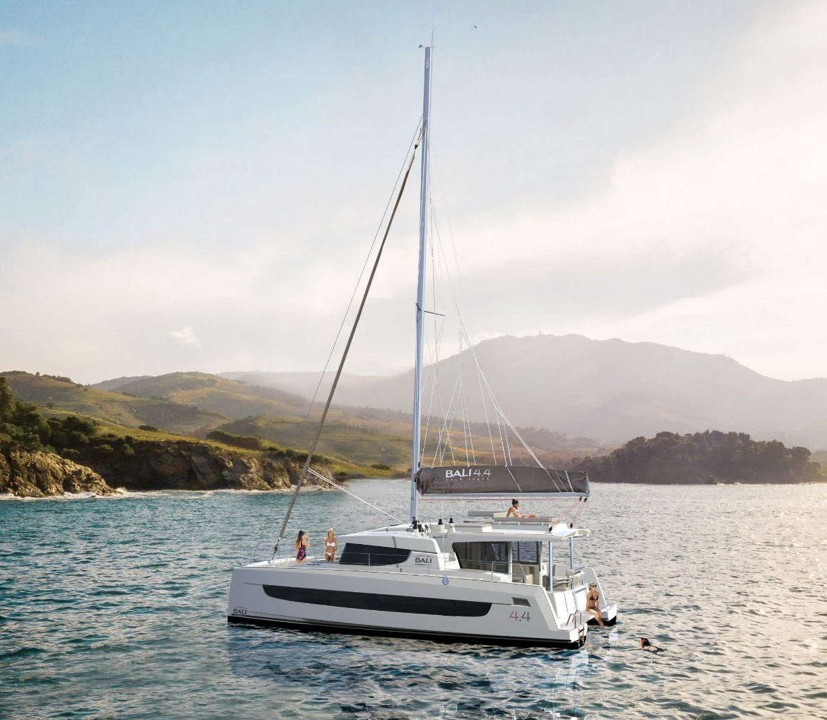 A catamaran glides gracefully across the ocean, its sails billowing in the wind under a clear blue sky.