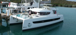 A catamaran is securely docked at a marina, surrounded by calm waters and a clear blue sky.