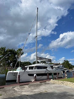 A catamaran is securely docked at a marina, surrounded by calm waters and other boats in the background.