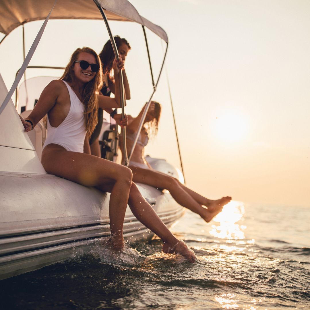 Three women in swimsuits enjoying a sunset on a boat, capturing a moment of relaxation and camaraderie.