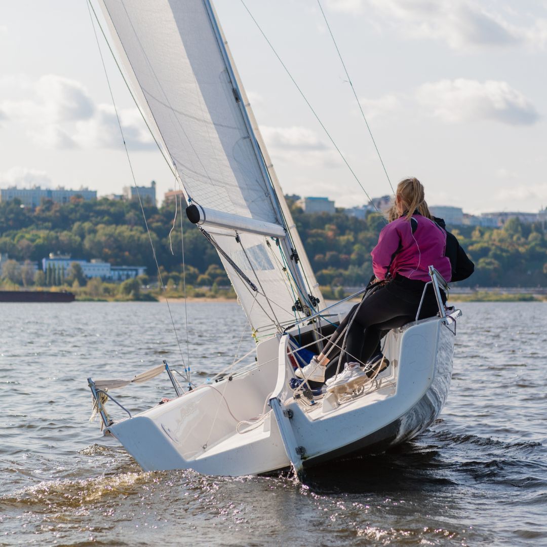 A woman sits at the bow of a sailboat, enjoying the serene view of the water and the open sky.