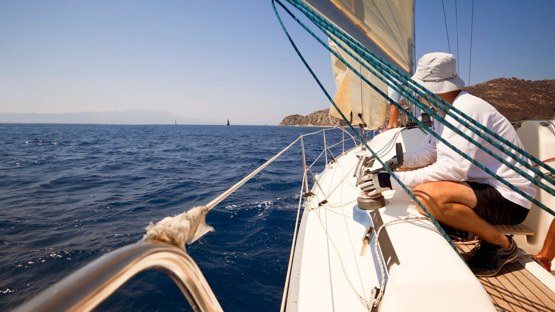 A man sits on the bow of a sailboat, enjoying the serene view of the water and the open sky.