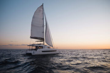 A catamaran gliding across the ocean, illuminated by the warm hues of a sunset in the background.