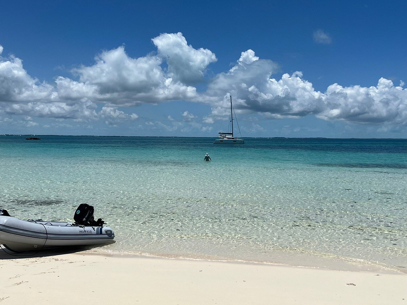 A boat rests on the beach beside another white boat, with sand and gentle waves in the background.