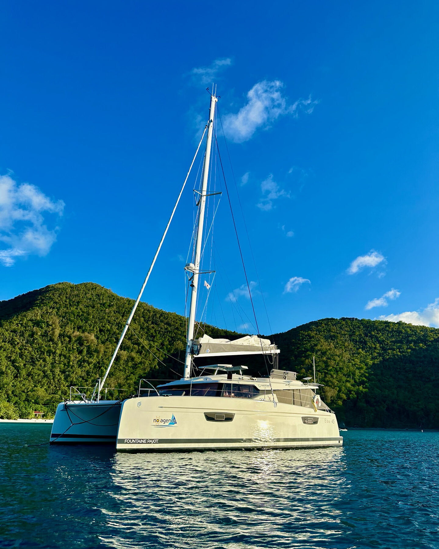 A catamaran glides through the ocean waters, with a majestic mountain rising in the background.