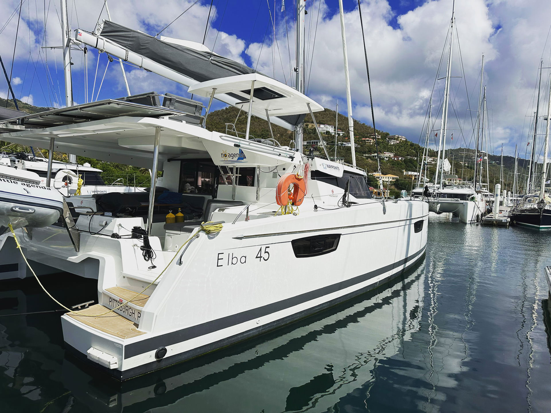 A catamaran is securely docked at the marina, surrounded by calm waters and a clear blue sky.