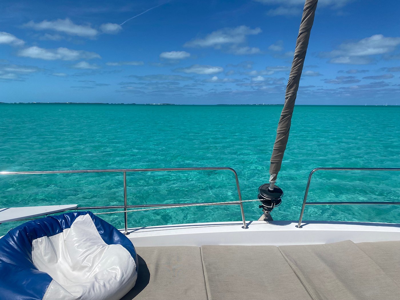 A serene view of the ocean stretching out from the deck of a boat, with gentle waves and a clear blue sky.