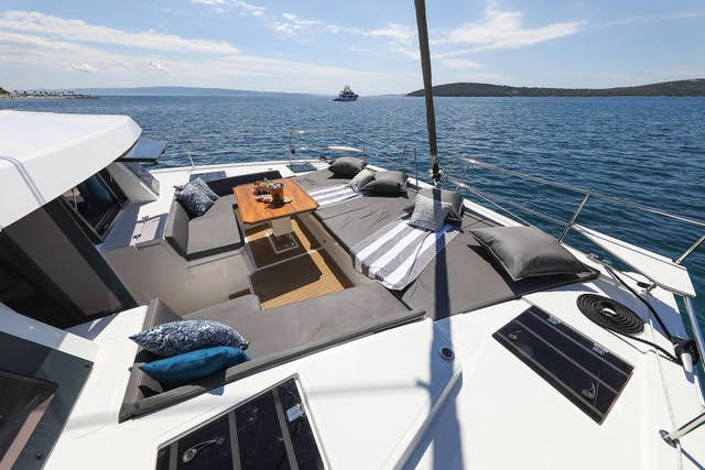 A sun deck on a catamaran boat, featuring lounge chairs and a panoramic view of the ocean under a clear blue sky.
