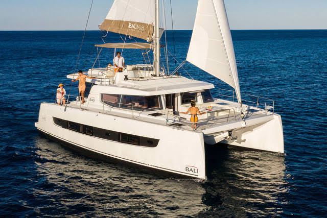 A catamaran navigates the open ocean, its sails billowing in the wind against a serene backdrop.