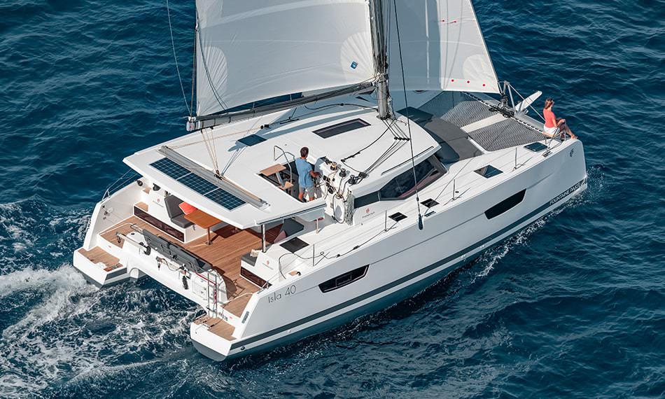 A catamaran navigates the open ocean, its sails billowing in the wind against a serene backdrop.