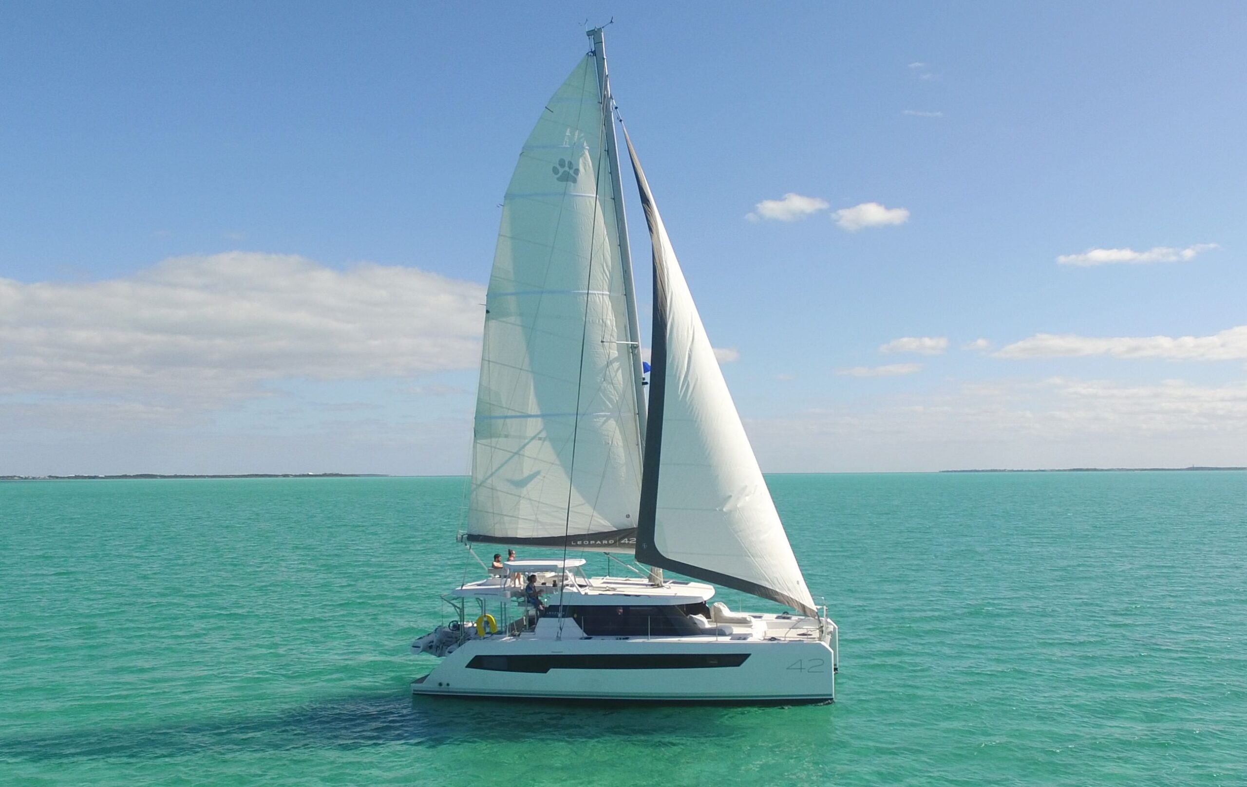 Serenity – Exterior 04 A catamaran gliding gracefully across the vast, open ocean under a clear blue sky.