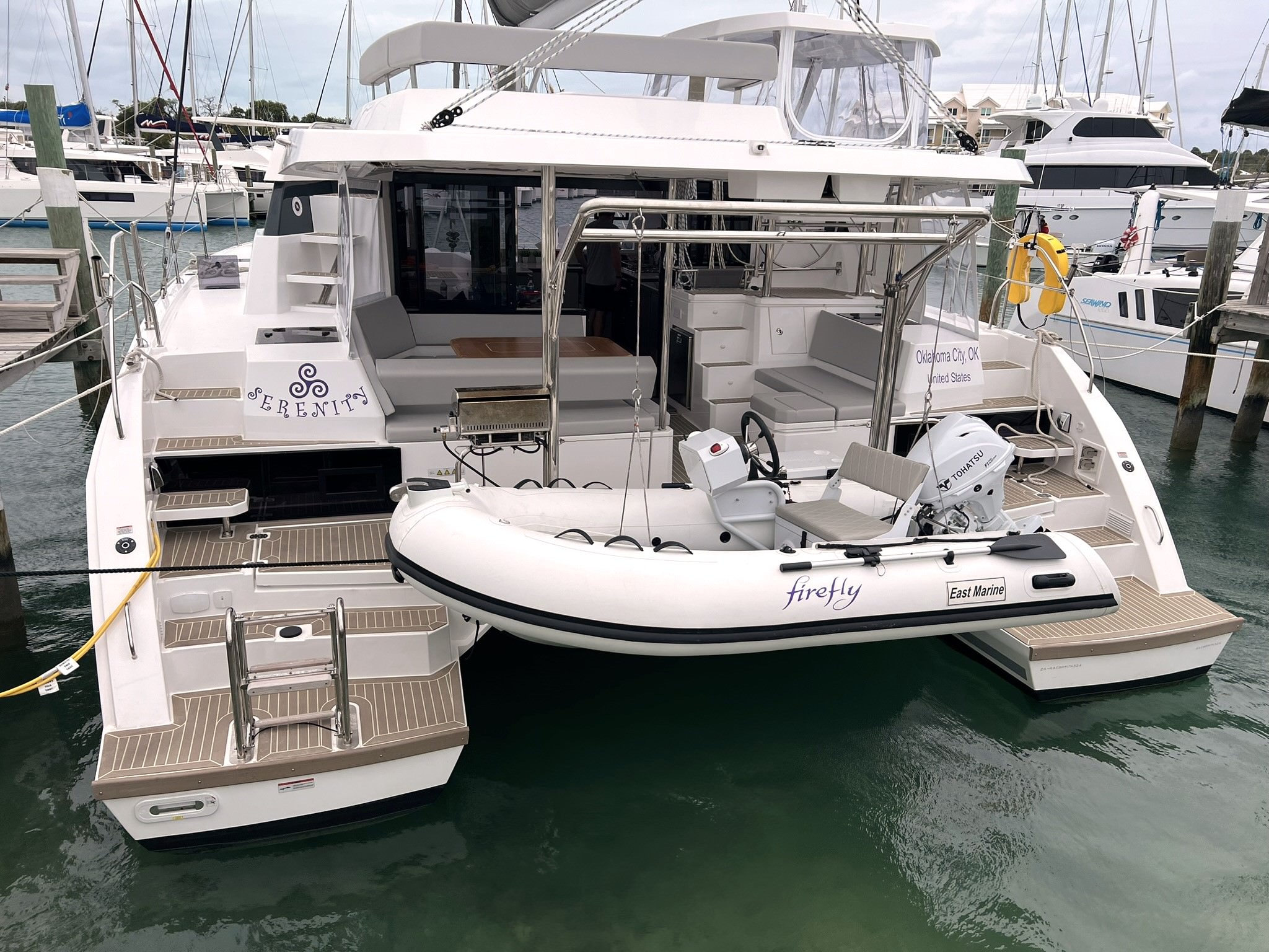 Serenity – Exterior 07 A catamaran anchored with a small boat securely tied alongside it, showcasing a serene maritime scene.