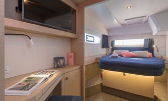 Interior view of a small boat, highlighting a bed and desk, designed for comfort and practicality in limited space.