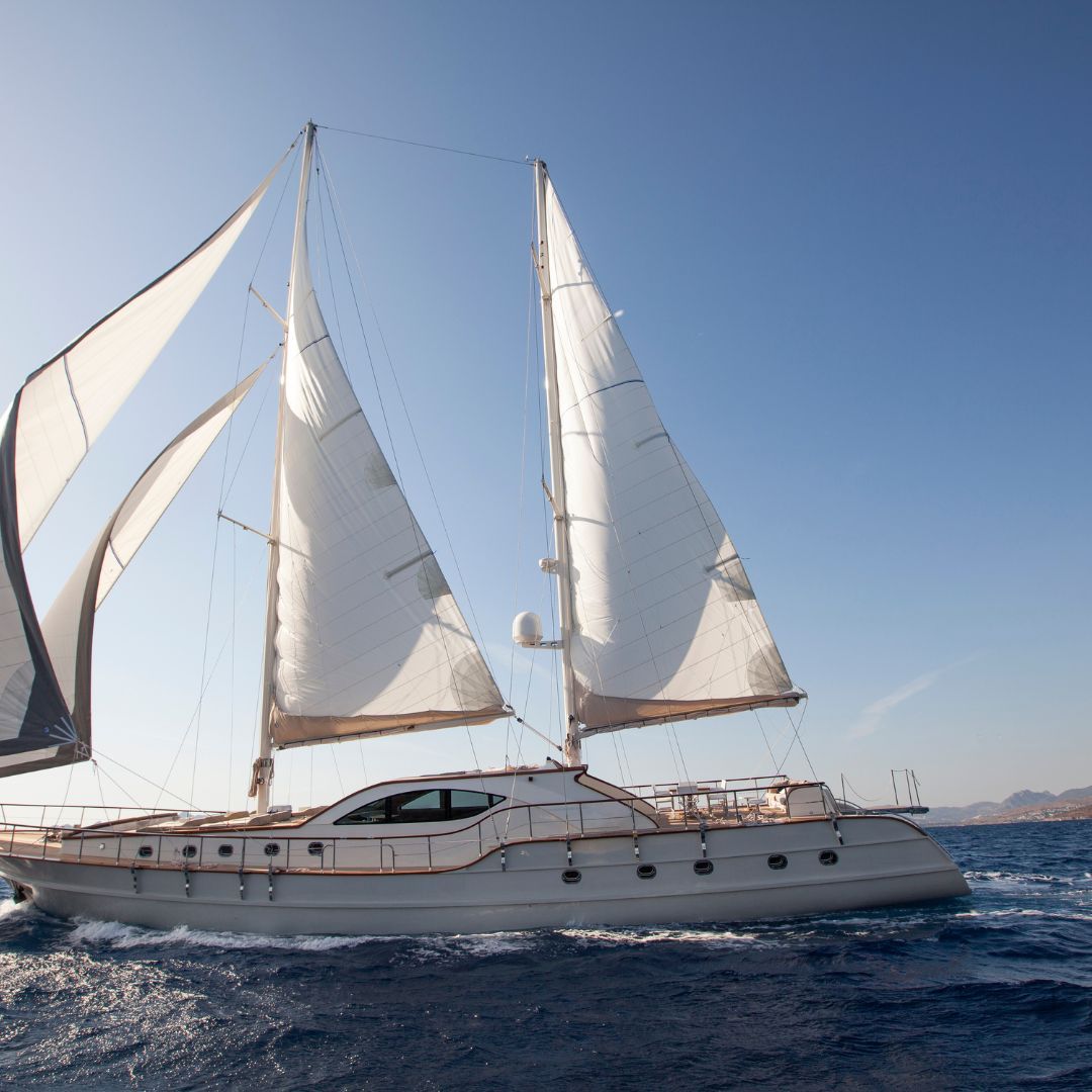 A sailboat with white sails glides gracefully across the blue ocean waters under a clear sky.