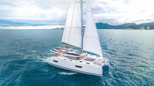 A catamaran gliding gracefully across the ocean, with waves gently lapping against its hull under a clear blue sky.