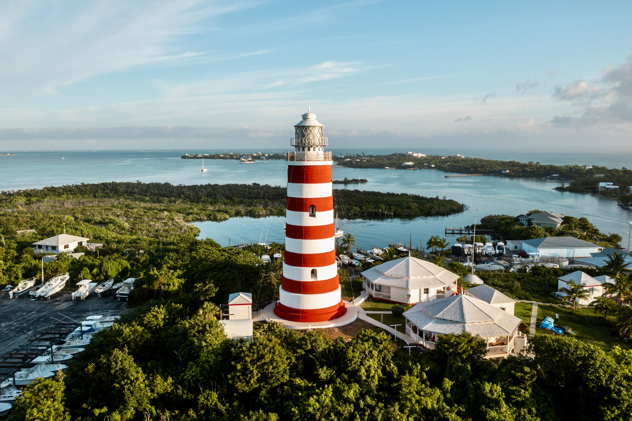 A red and white lighthouse stands atop a grassy hill, overlooking the surrounding landscape under a clear blue sky.
