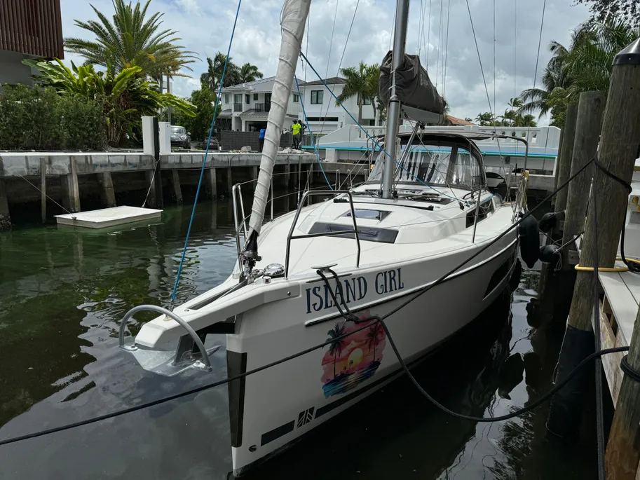 A sailboat is moored at a dock, gently bobbing on the water's surface under clear skies.