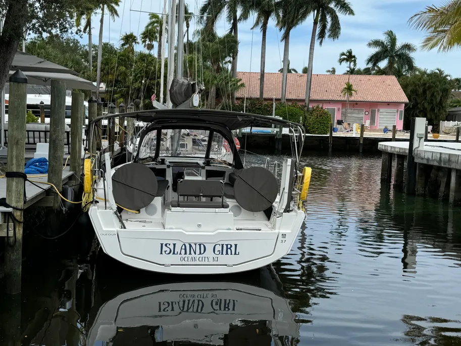 A sailboat rests at a dock, framed by tall palm trees swaying gently in the breeze.