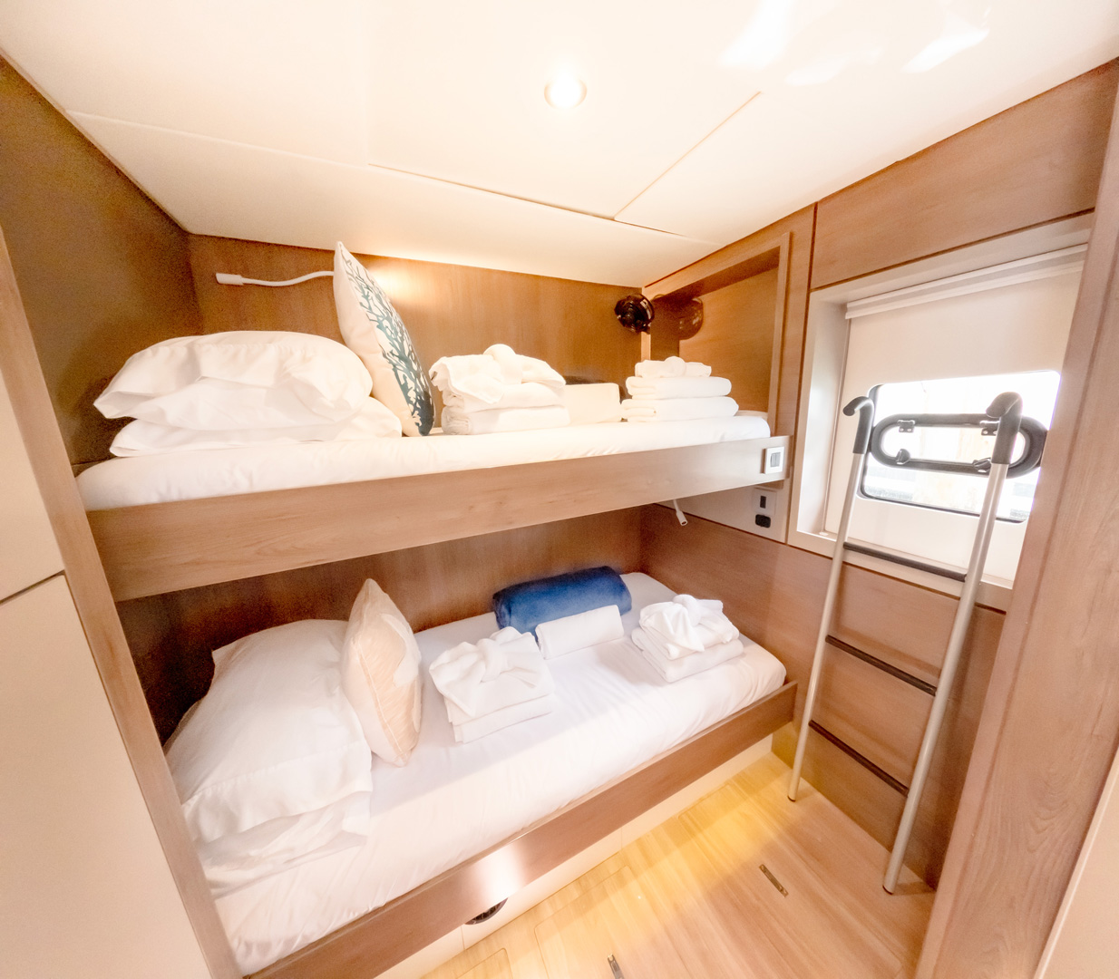 A small yacht cabin featuring a bunk bed, a single bed, and a desk, maximizing space in a compact environment.