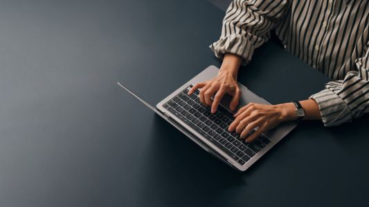  A person focused on typing on a laptop computer, with hands positioned on the keyboard and a screen illuminated.