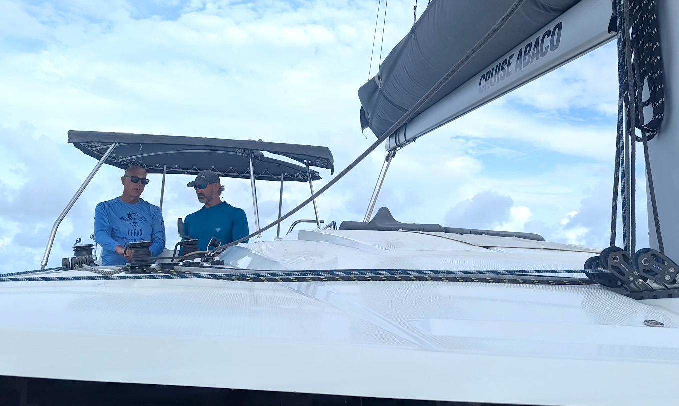 A boat rests on the beach beside another white boat, with sand and gentle waves in the background.