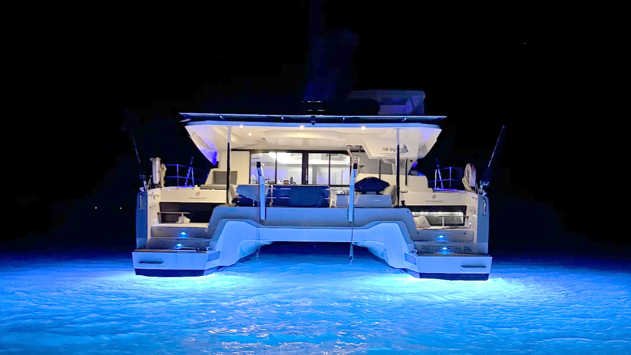 A boat rests on the beach beside another white boat, with sand and gentle waves in the background.