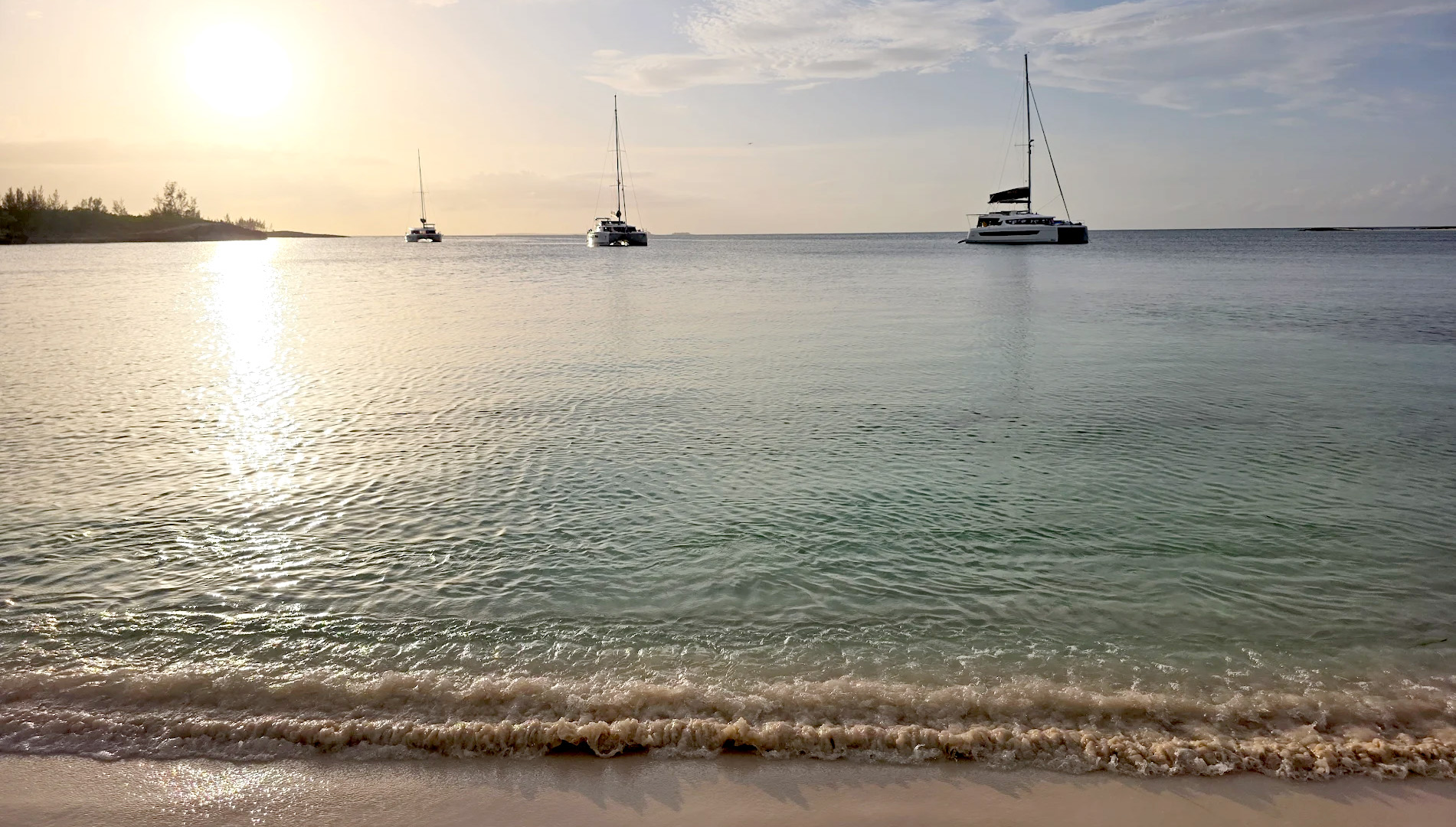 A boat rests on the beach beside another white boat, with sand and gentle waves in the background.