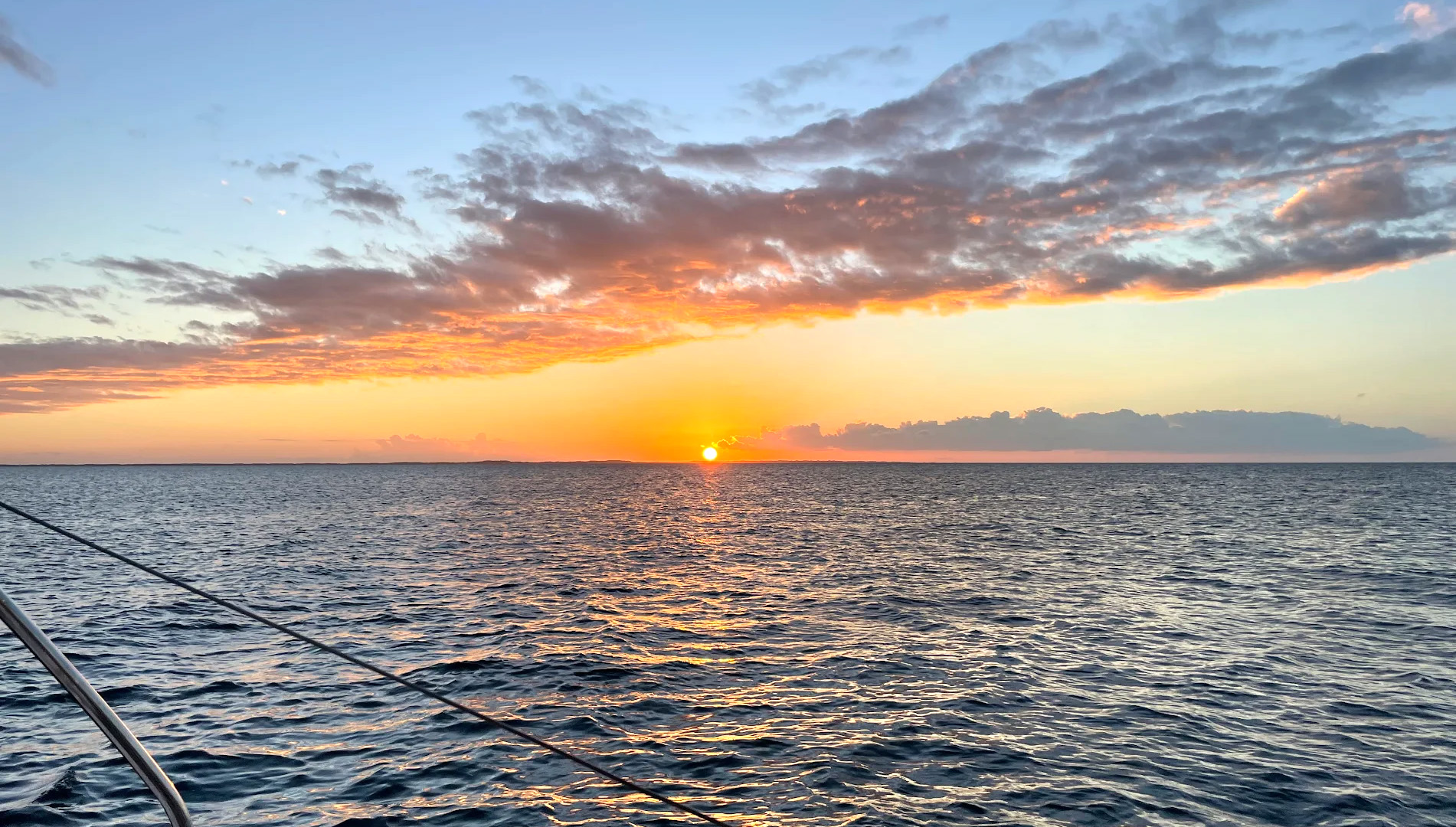 A boat rests on the beach beside another white boat, with sand and gentle waves in the background.